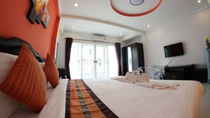 A hotel room with a large bed, a flat-screen TV, a desk, and a view of the city through the window. - Tulip Inn (Patong)