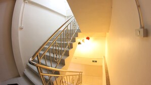 A spiral staircase with a metal railing, a wall-mounted light fixture, and a sign indicating the direction to the elevator. - Tulip Inn (Patong)