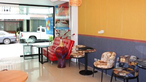 A hotel lobby with a red sofa, a large vase, and a table with chairs. A white car is parked outside. - Tulip Inn (Patong)