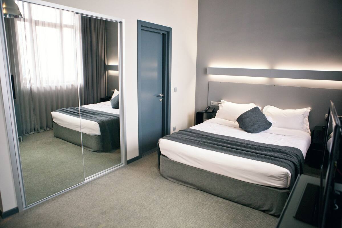 A hotel room with a bed, bedside table, lamp, and a mirror.