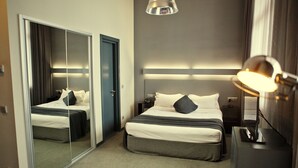 Ein Hotelzimmer mit großem Spiegel, einem Bett mit weißer Bettwäsche, einem Nachttisch mit Lampe und einem Kleiderschrank.