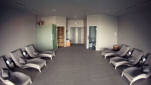Ein Wellnessbereich mit mehreren Liegestühlen, die halbkreisförmig angeordnet sind, einem Empfangstresen und einer Holztür zu einem weiteren Raum.