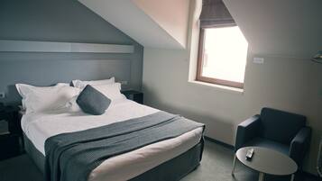 Una habitación de hotel con una cama, una silla, una mesita y una ventana.