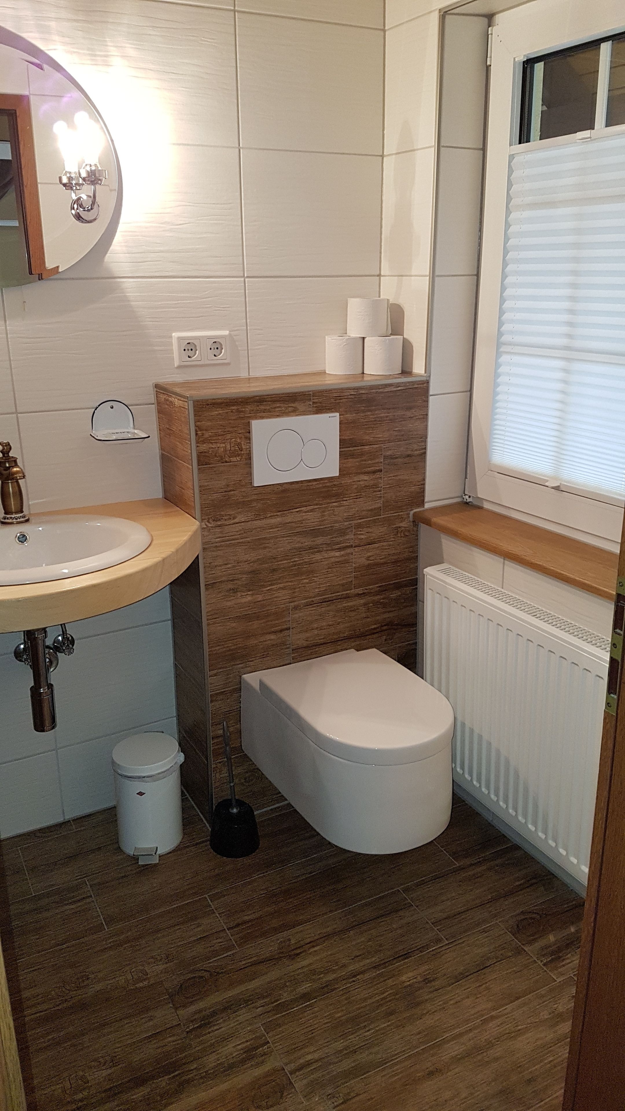 A compact bathroom with a wooden vanity, a white toilet, and a radiator.