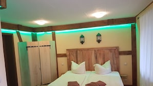 Una cama de madera con ropa de cama blanca, dos lámparas de pared y una tira de luces LED verdes a lo largo del techo.