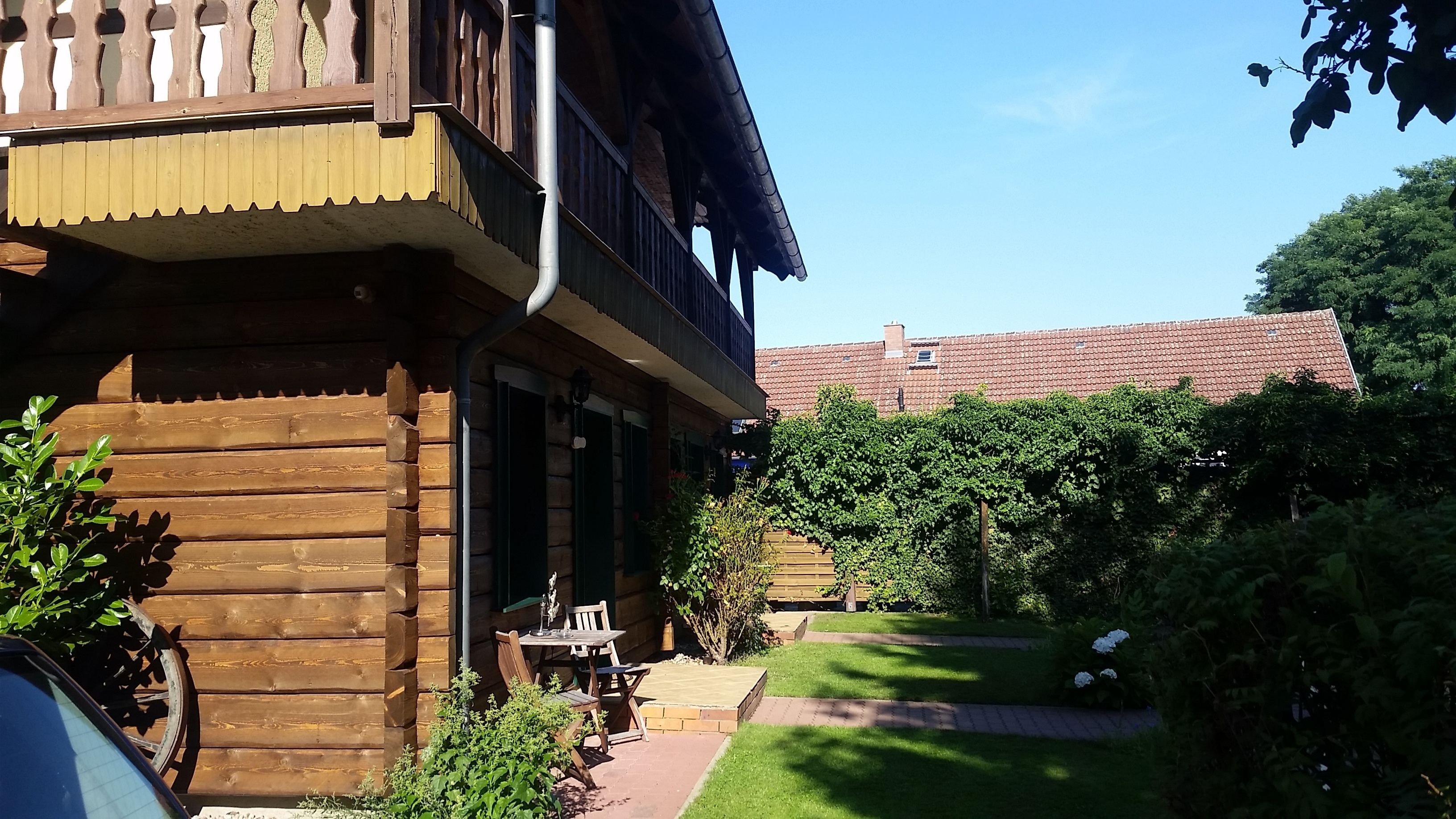 A wooden cabin with a balcony, a small outdoor seating area, and a well-maintained garden.