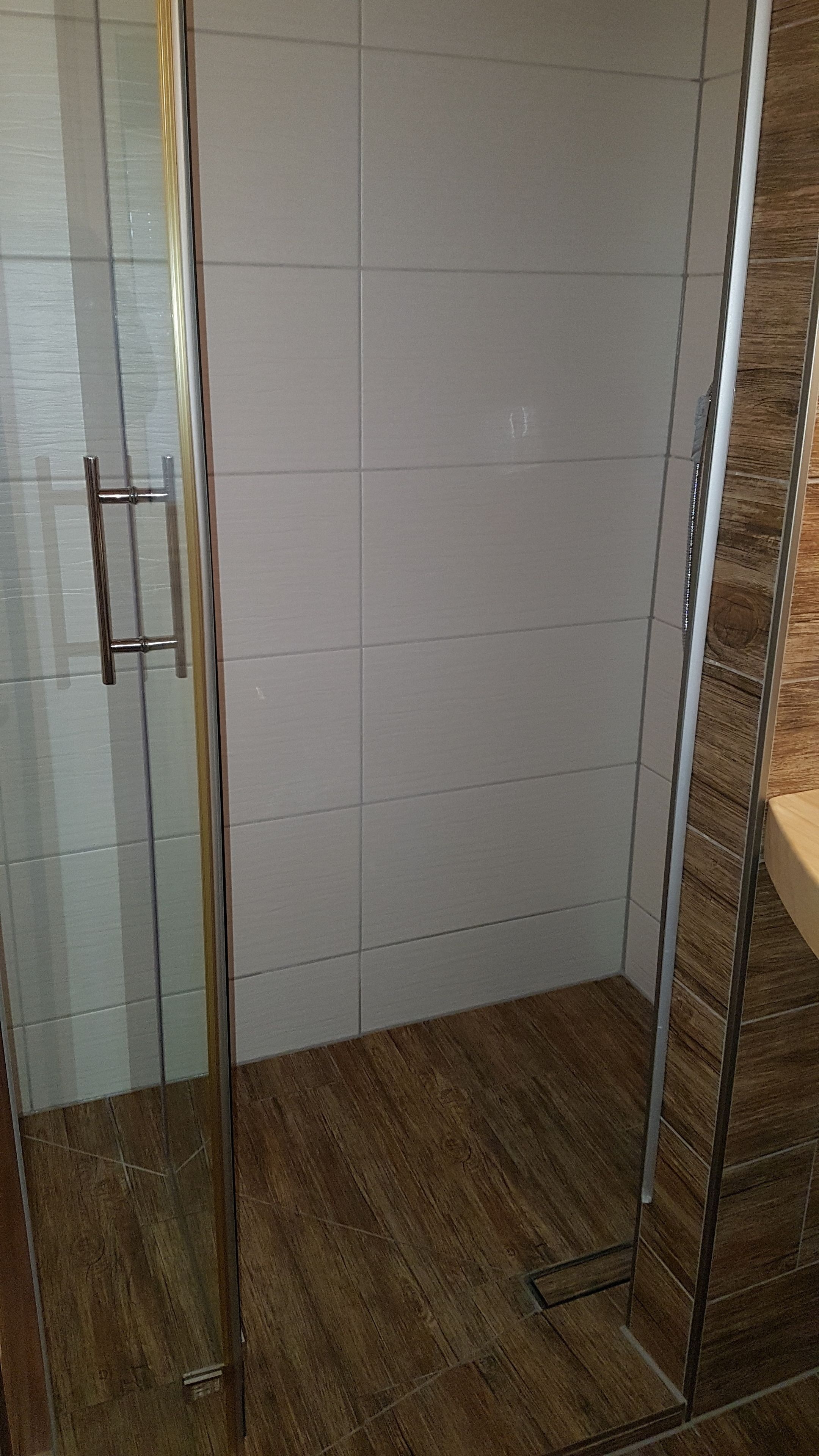 A shower area with a glass door, tiled walls, and a wooden floor.