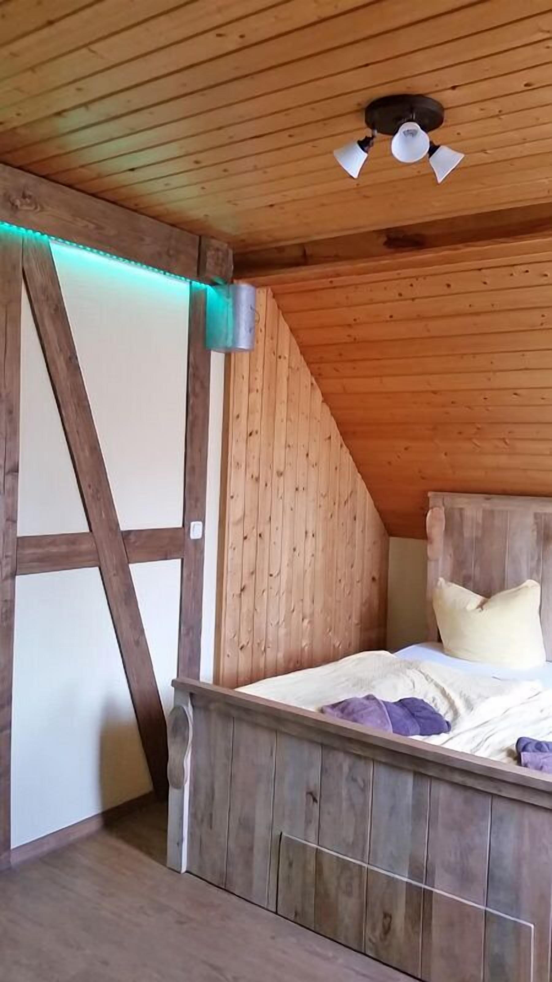 A bedroom with wooden walls, a sloped ceiling, a bed with a headboard, and a ceiling fan.