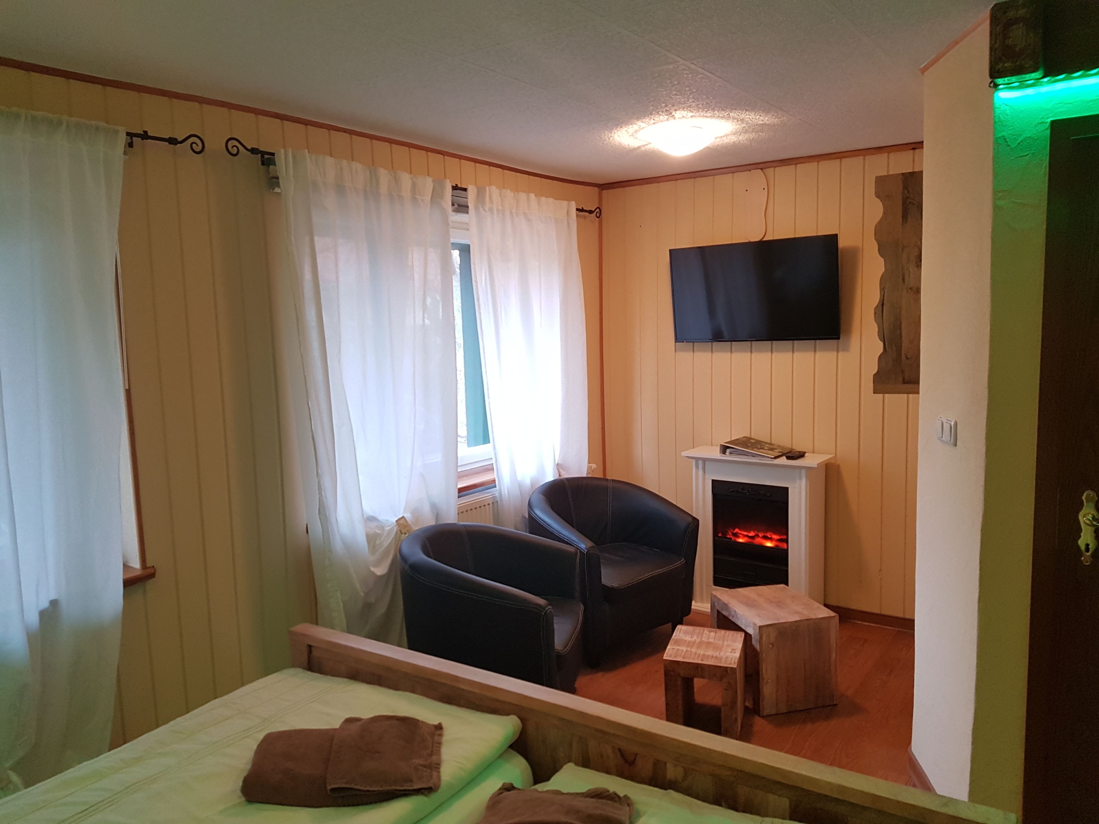 A room with a bed, a chair, a small table, a fireplace, and a TV mounted on the wall.
