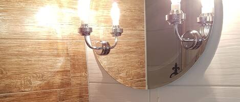 A bathroom with a wooden vanity, a white sink, a mirror, and a wall-mounted light fixture.