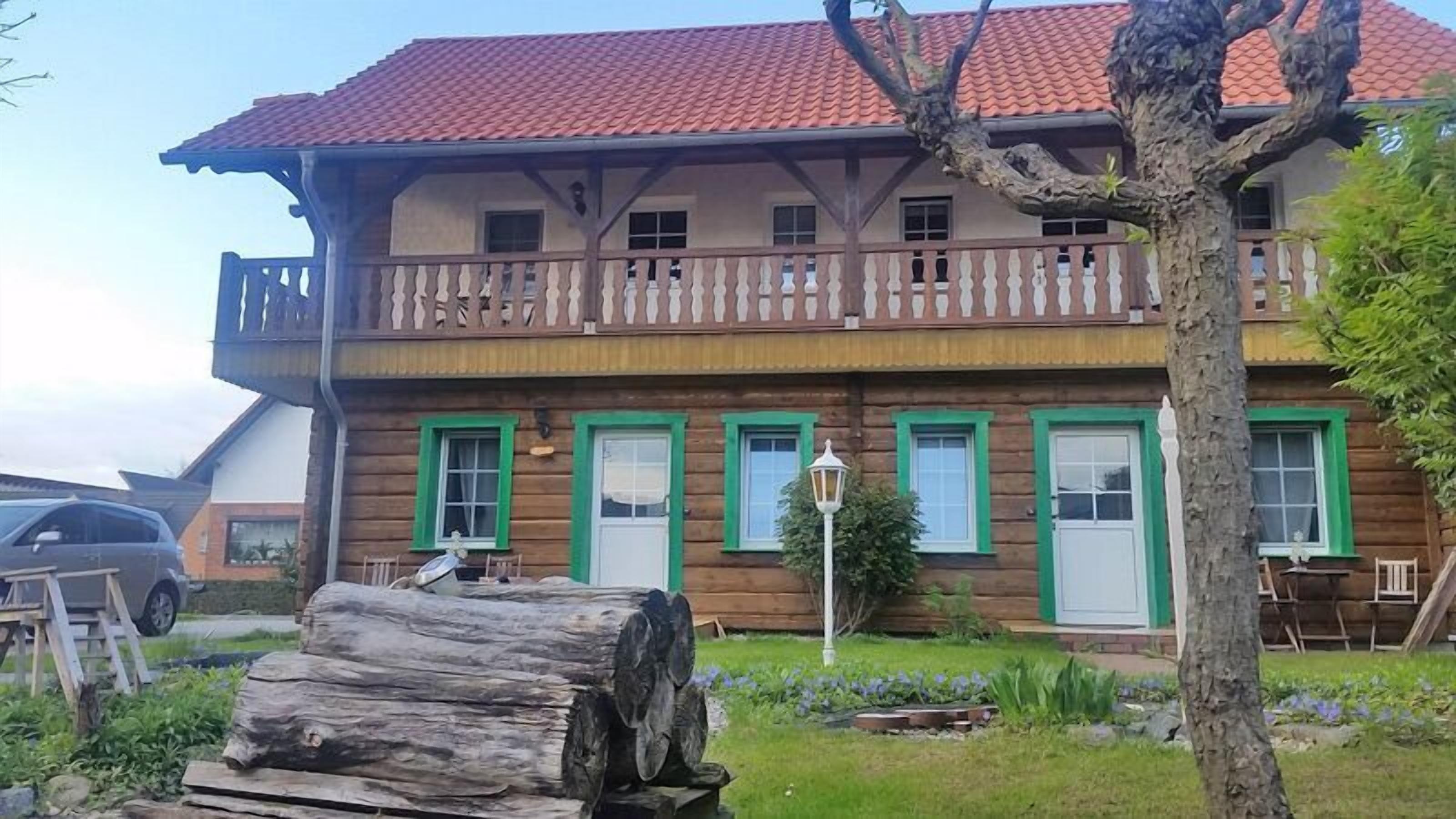 Una casa de madera de dos pisos con balcón y ventanas con marco verde.