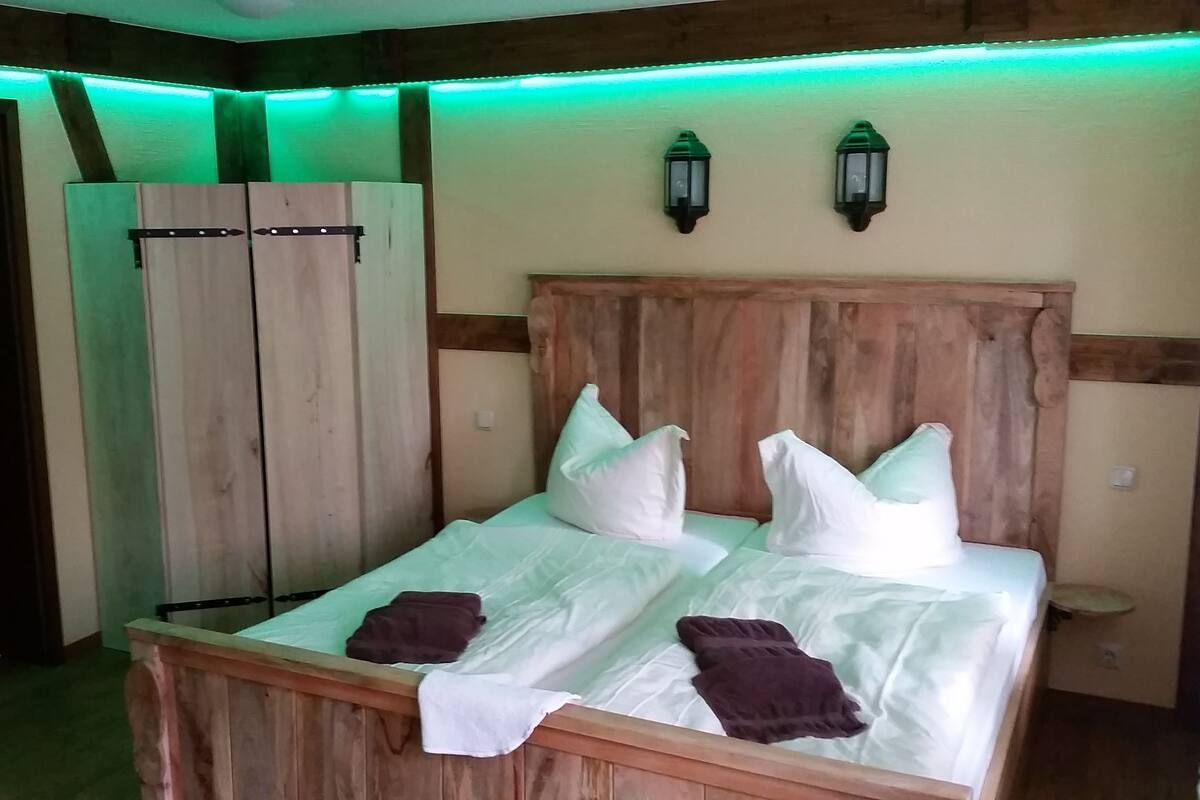 Una cama de madera con almohadas blancas y marrones, un cabecero de madera y dos lámparas de pared.