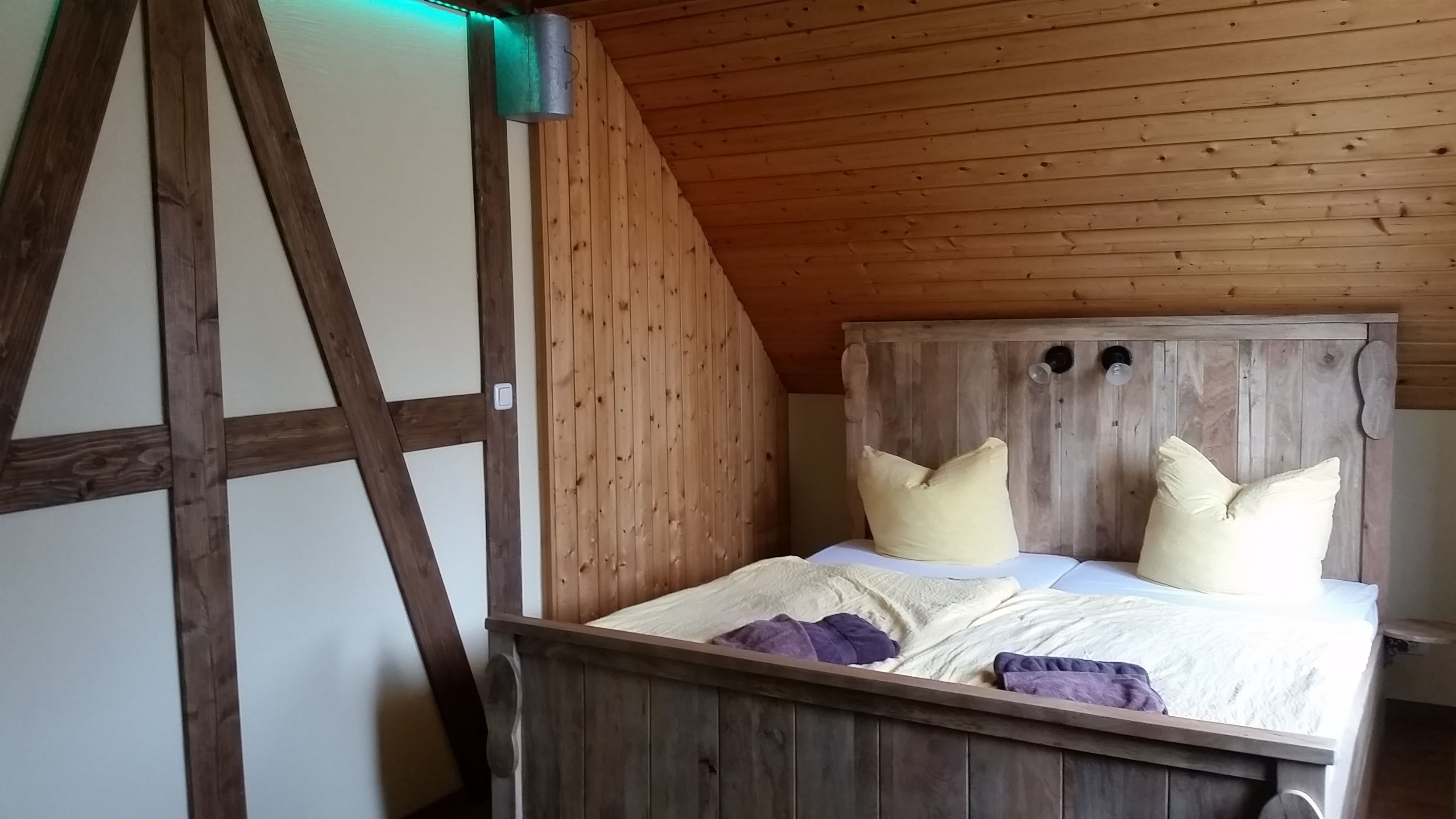 A wooden bed with a sloped ceiling, a wooden headboard, and two pillows.