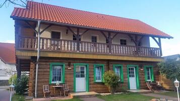 Een tweelaags houten huis met een balkon, groene raamkozijnen en een rode pannendak.