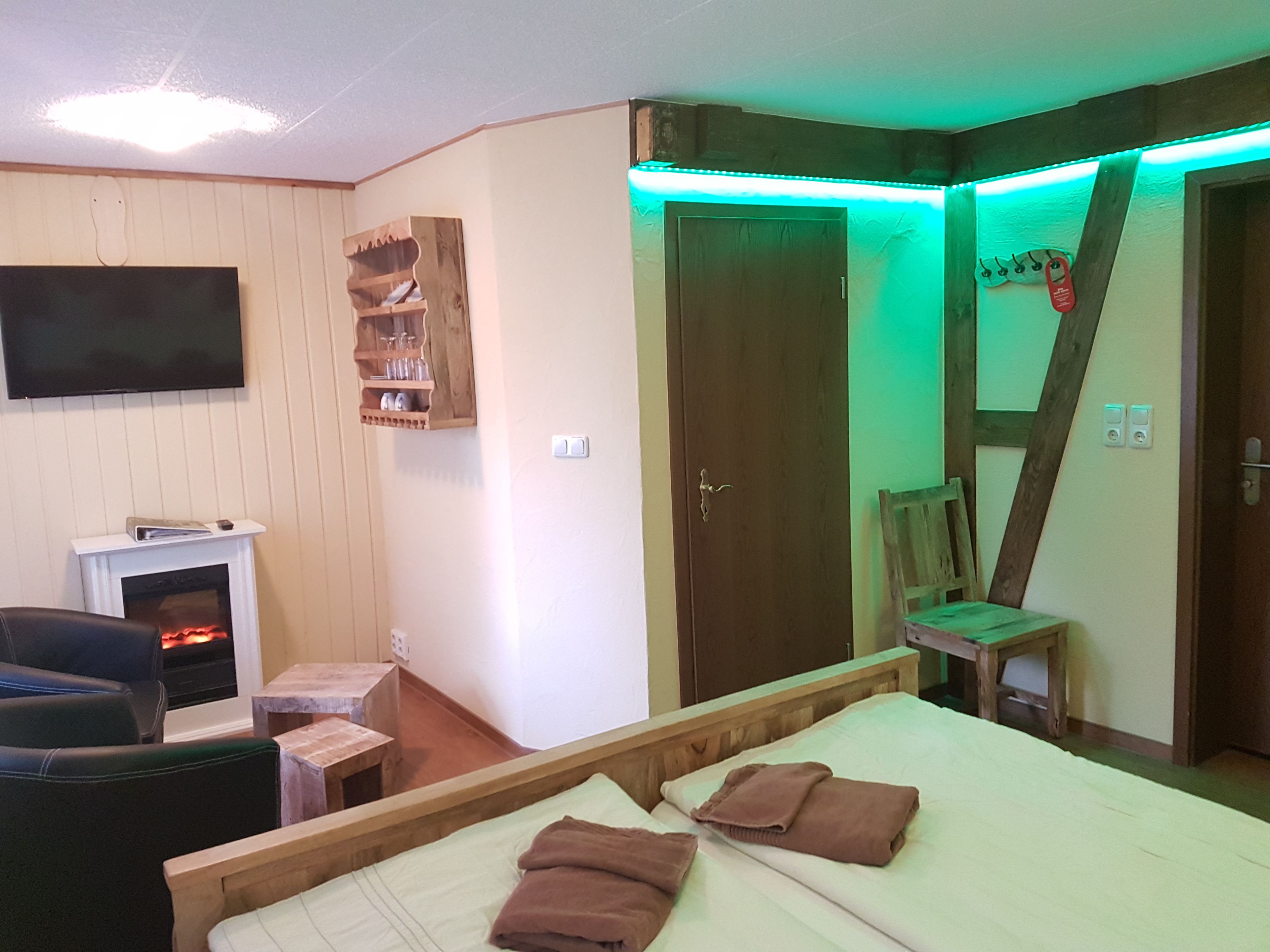 Un dormitorio con cama, una silla, una mesita, una chimenea y un televisor montado en la pared.