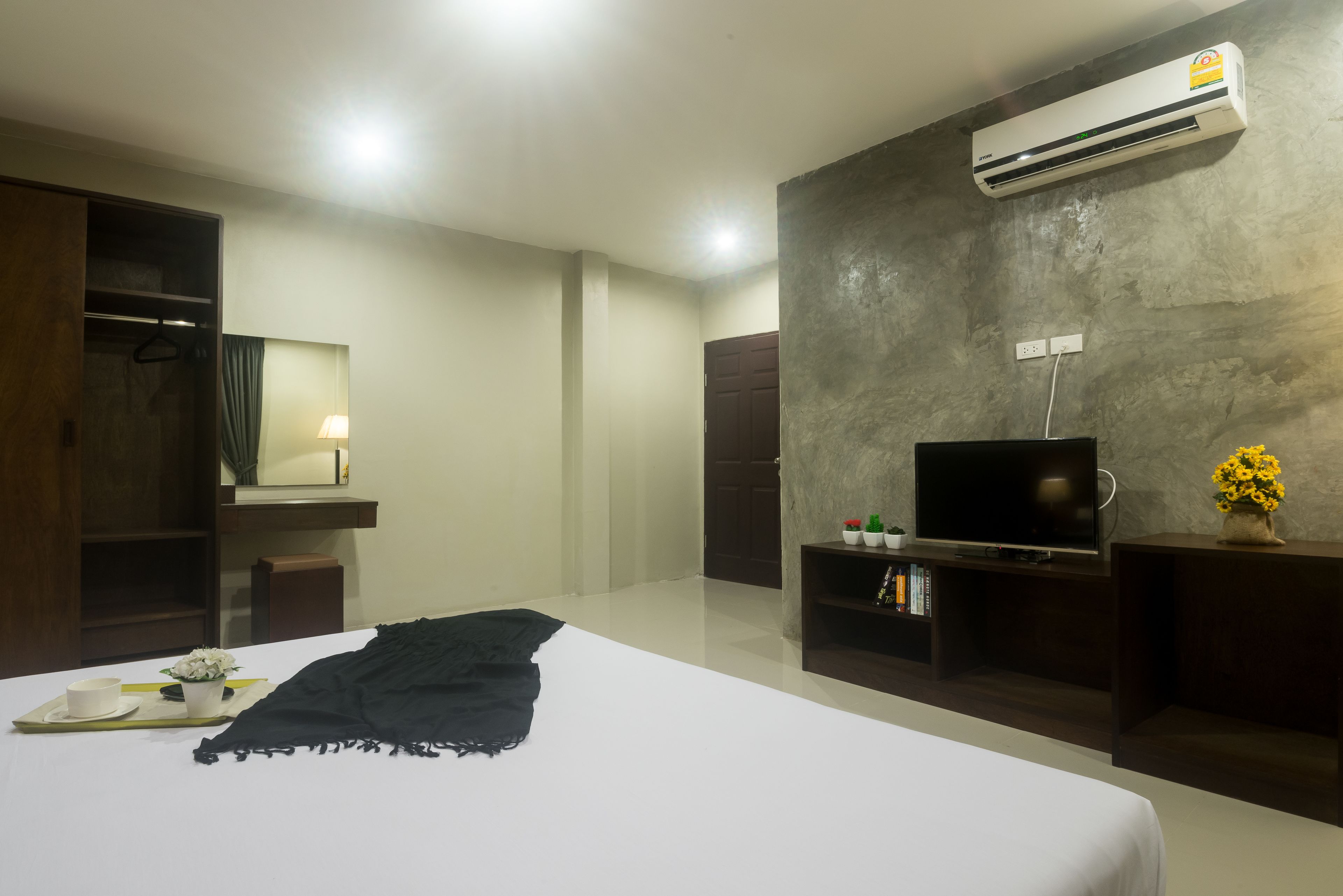 Quarto de hotel moderno com cama, televisão, guarda-roupa, espelho e unidade de ar condicionado.