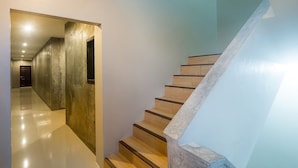 A modern staircase with wooden steps and a concrete handrail, leading to a hallway with a polished floor and a door at the end.
