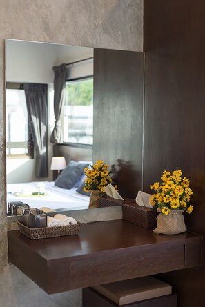 A modern bathroom with a large mirror, a wooden vanity, and a vase of yellow flowers. - Green Leaf Hostel (Phuket)