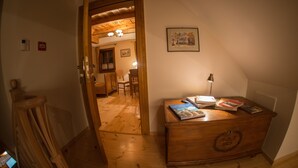 A wooden dresser with books and a lamp, a wooden floor, a framed picture on the wall, and a door leading to another room.