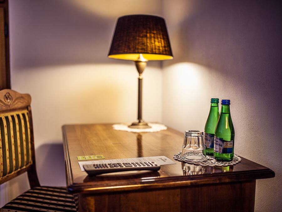 A wooden desk with a lamp, two green bottles, a glass, and a keyboard.