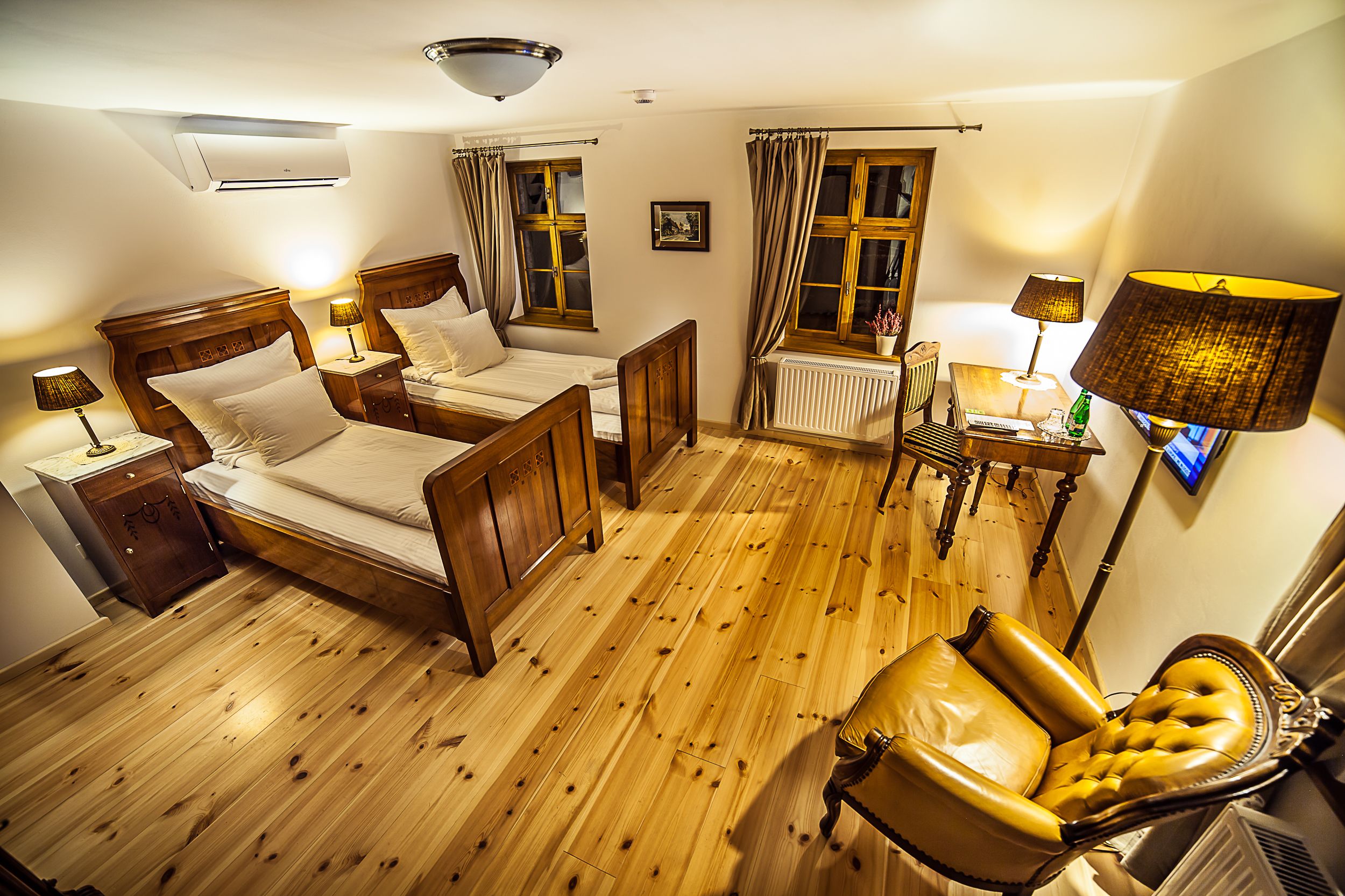 Ein Zimmer mit zwei Holzbetten, einem Ledersessel, Holzdielen, einer Heizung und einem an der Wand befestigten Fernseher.