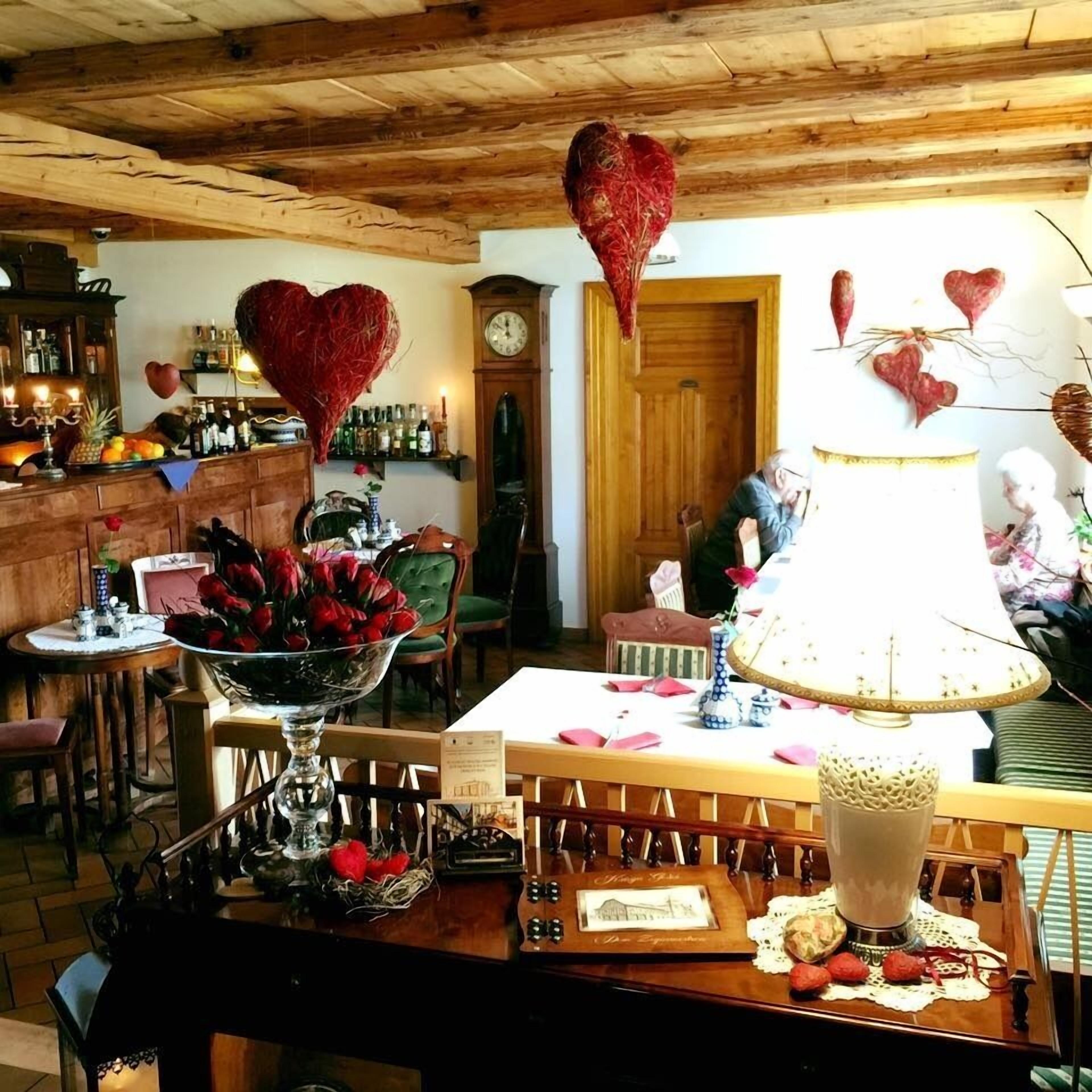 Una habitació acollidora amb bigues de fusta al sostre, una zona de bar amb ampolles, una taula amb un ram de flors vermelles i una lampada blanca gran.