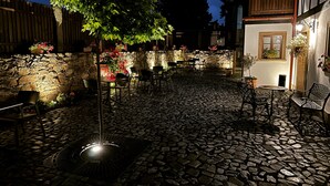 A cobblestone courtyard with outdoor seating, a stone wall, and a tree providing shade.