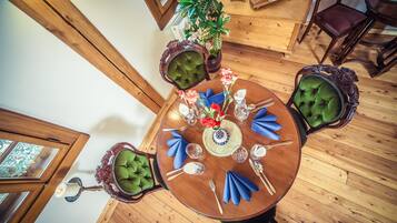A round wooden dining table with green upholstered chairs, set with blue napkins, silverware, and a vase of flowers.