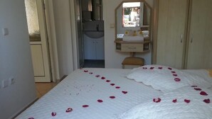 A bedroom with a bed covered in rose petals, a mirror above the dresser, and a door leading to a bathroom. - Cennet Apart (Bodrum)