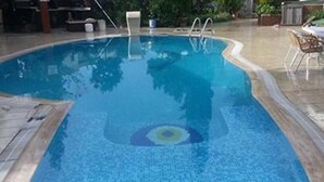 A swimming pool with a clear blue center, surrounded by a tiled deck and a lounge area with chairs. - Cennet Apart (Bodrum)