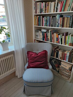 Un sillón a rayas con un cojín rojo en una habitación con una estantería llena de libros.