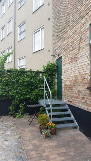A brick building with a green door, a metal staircase, and a small garden area with potted plants. - Lilla Hotellet (Lund)