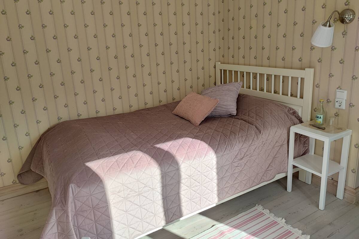 Un dormitorio con cama, mesita de noche, lámpara y enchufe en la pared.