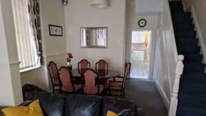 A living room with a black leather sofa, yellow cushions, a dining table with chairs, a mirror, and a staircase leading to another area. - Fern Lodge (Preston)