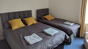 Two twin beds with grey headboards and brown bedding, each with a yellow pillow and a folded white towel. - Fern Lodge (Preston)