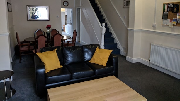 A living room with a black leather sofa, a wooden coffee table, a dining area with a table and chairs, and a staircase leading to another floor. - Fern Lodge (Preston)