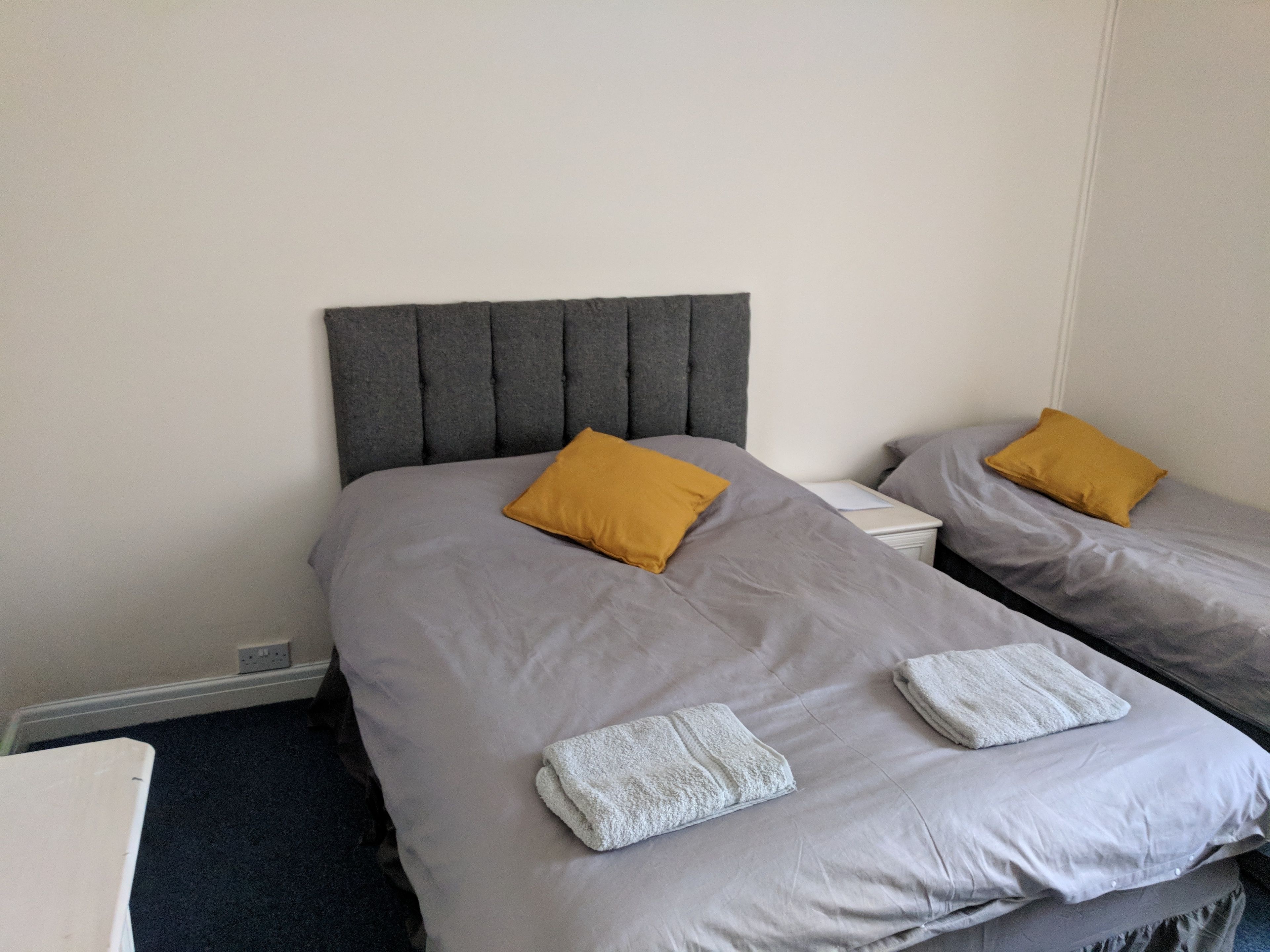 A hotel room with two beds, each with a grey headboard and a mustard-colored pillow. There are white towels on the beds.