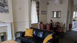 A living room with a black leather sofa, a wooden coffee table, a fireplace, a dining area with a table and chairs, and a kitchen visible in the background. - Fern Lodge (Preston)