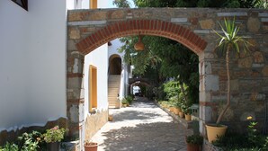 Un sendero de piedra bordeado por plantas en macetas y un arco de ladrillo que conduce a un edificio.