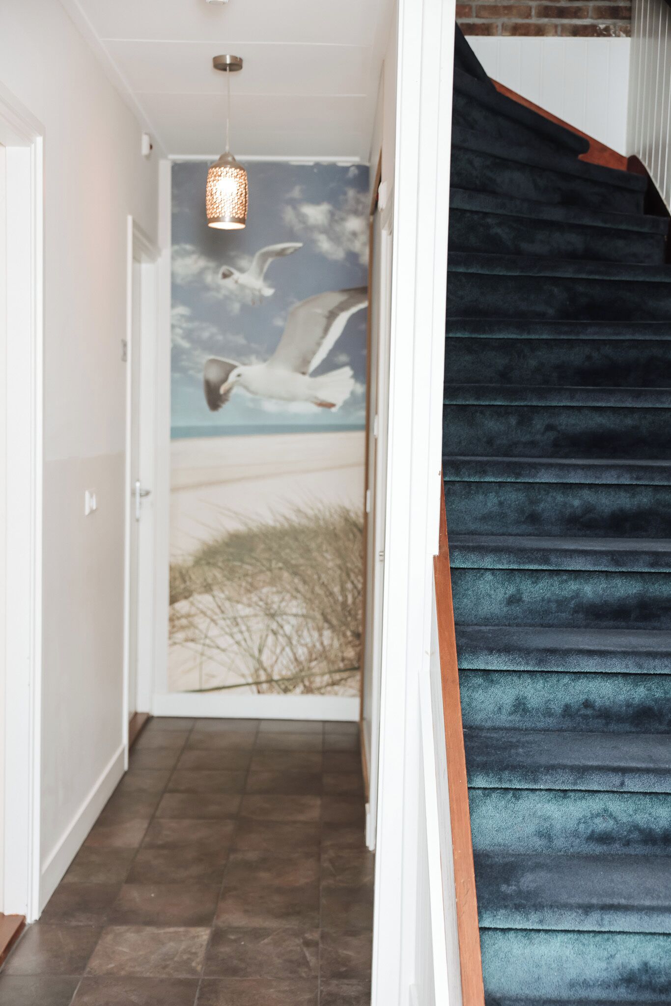 Un escalier aux marches sombres et une fresque murale représentant des mouettes volant au-dessus d’une plage.