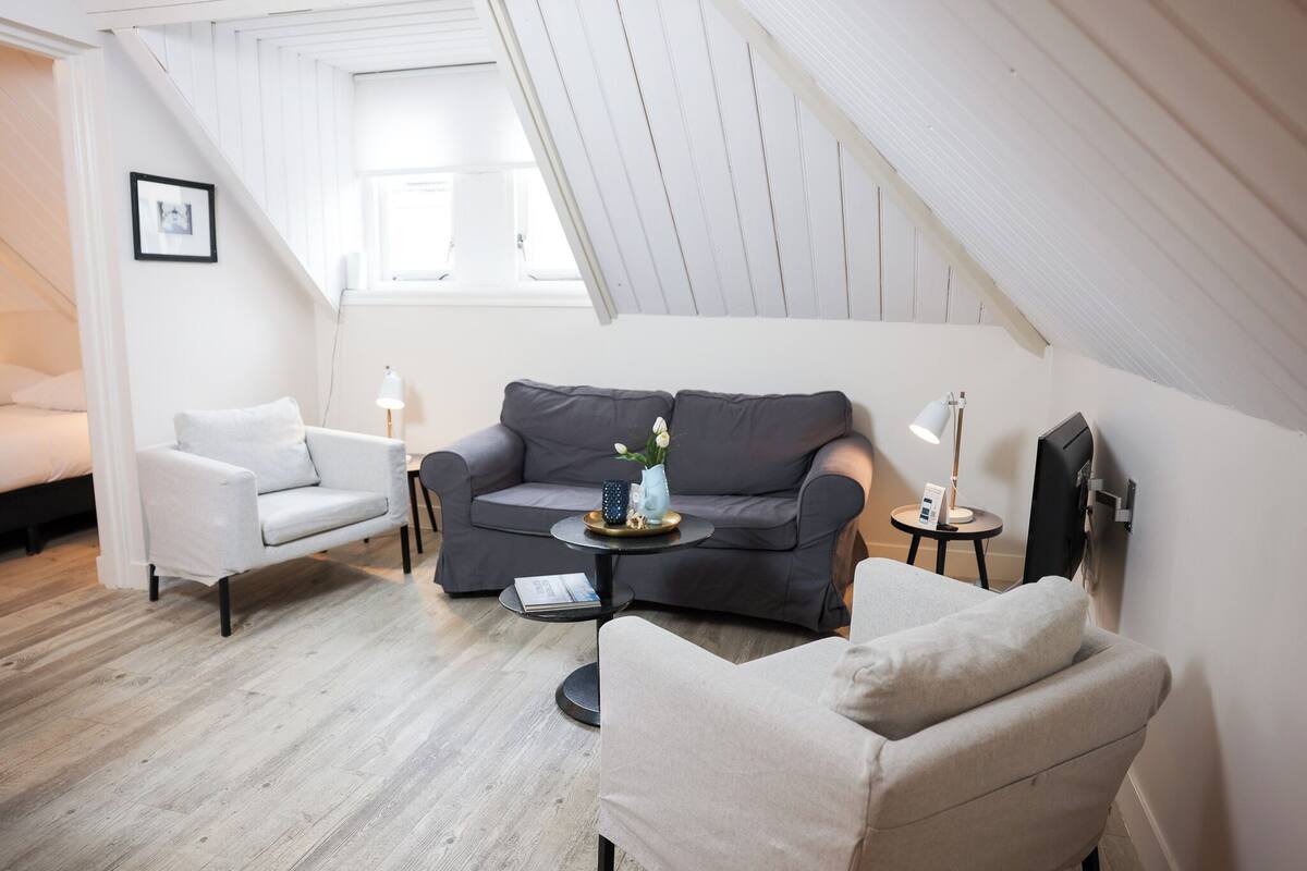 Ein modernes Wohnzimmer mit grauem Sofa, weißen Sesseln und einem kleinen runden Tisch mit Dekorationen.