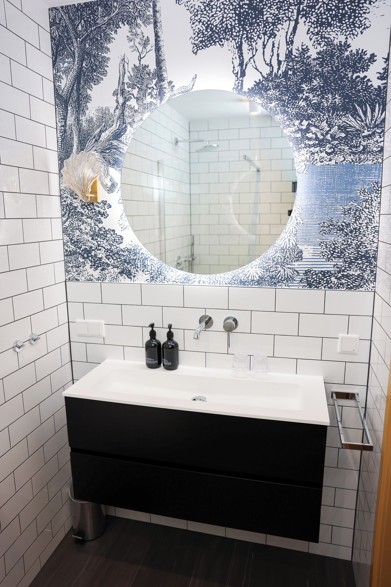 A bathroom with a white sink, black cabinet, and a large mirror with a blue and white tree pattern.