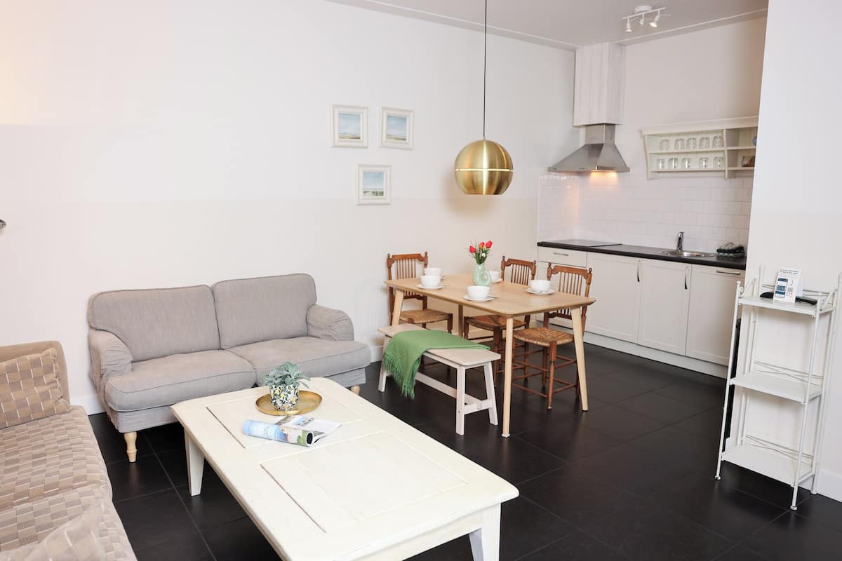 Ein modernes Wohnzimmer mit Sofa, Couchtisch und Esstisch. Es gibt eine Küchenzeile mit Schränken und einer Pendelleuchte.