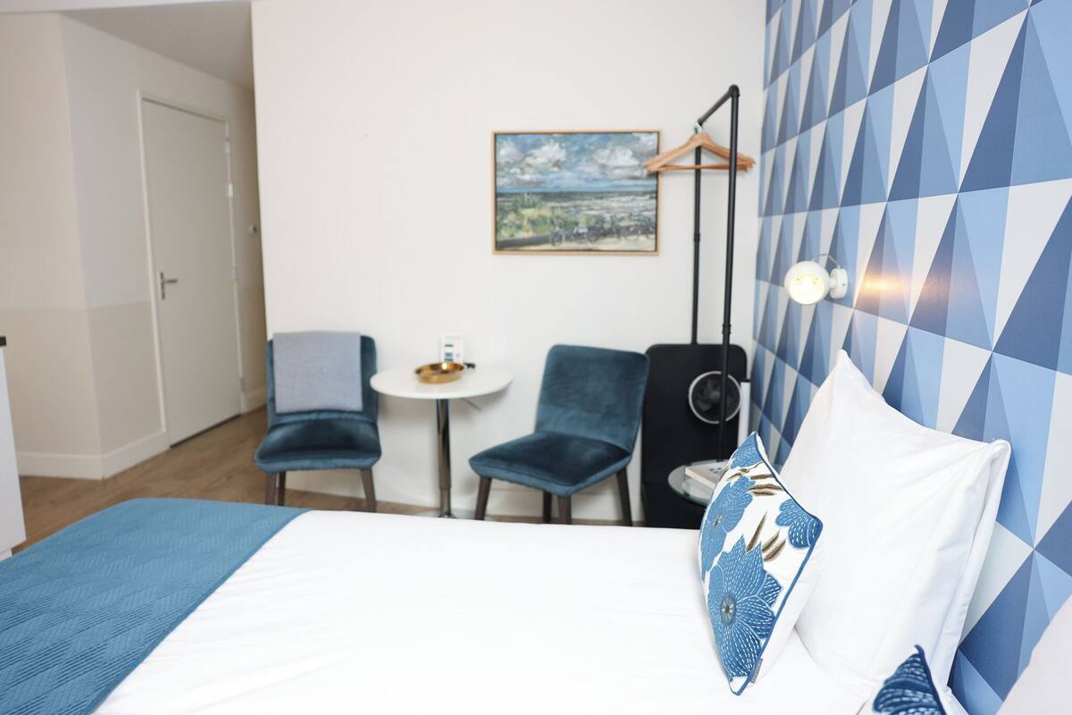 Ein Hotelzimmer mit einem Bett, einem kleinen runden Tisch, zwei Stühlen, einem an der Wand befestigten Fernseher und einem Bild an der Wand.