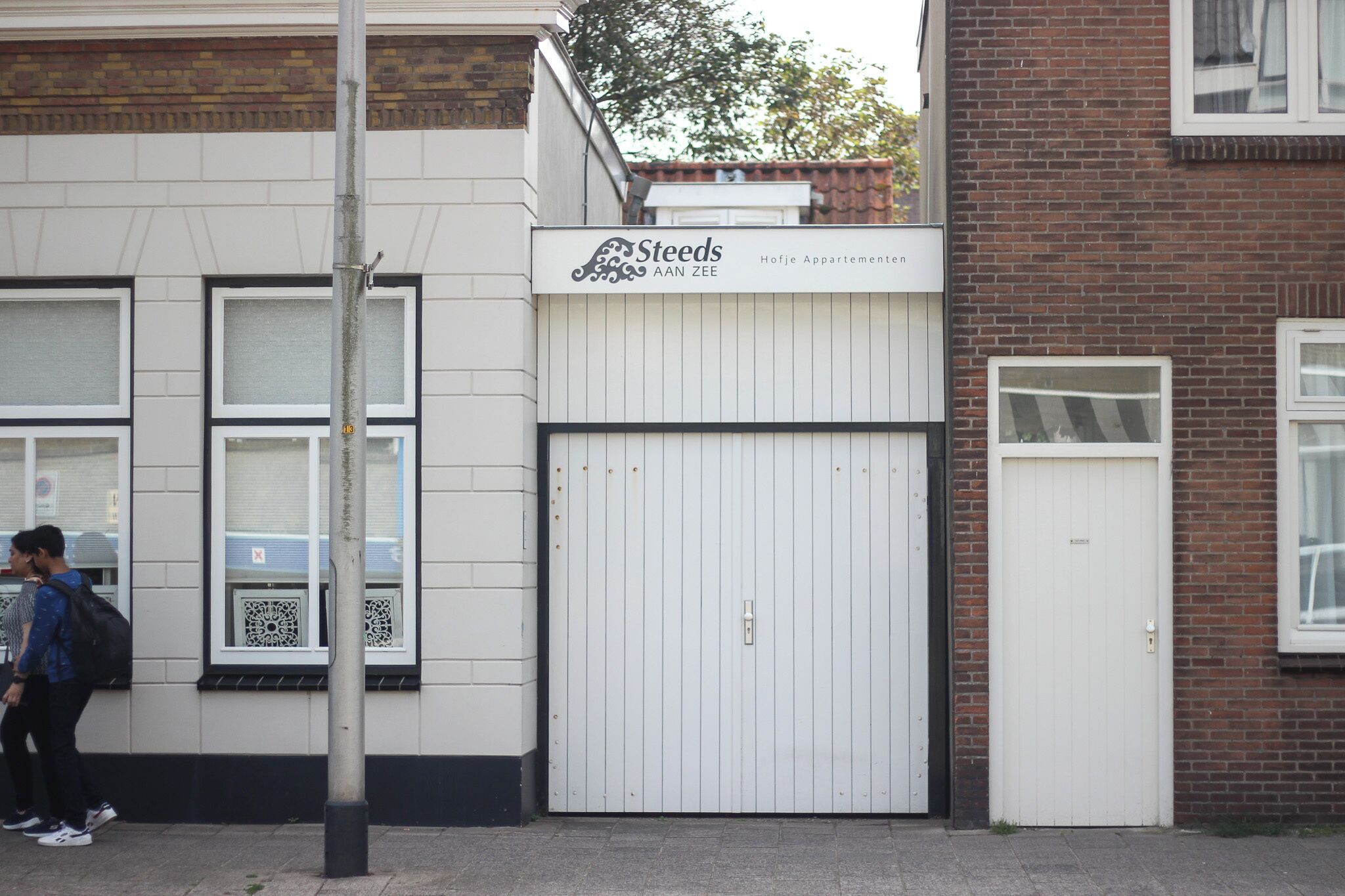 Een gebouw met een bord waarop staat 'Steeds AAN ZEE' en een gesloten witte garage deur.
