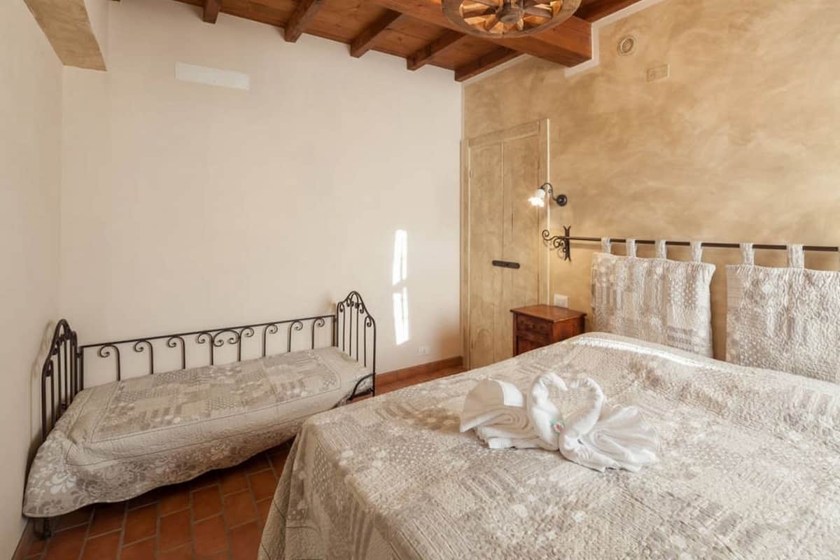 A bedroom with two single beds, a wooden ceiling, a tiled floor, and a plain wall.