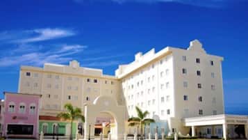 A multi-story hotel with a central archway, multiple balconies, and a clear blue sky.