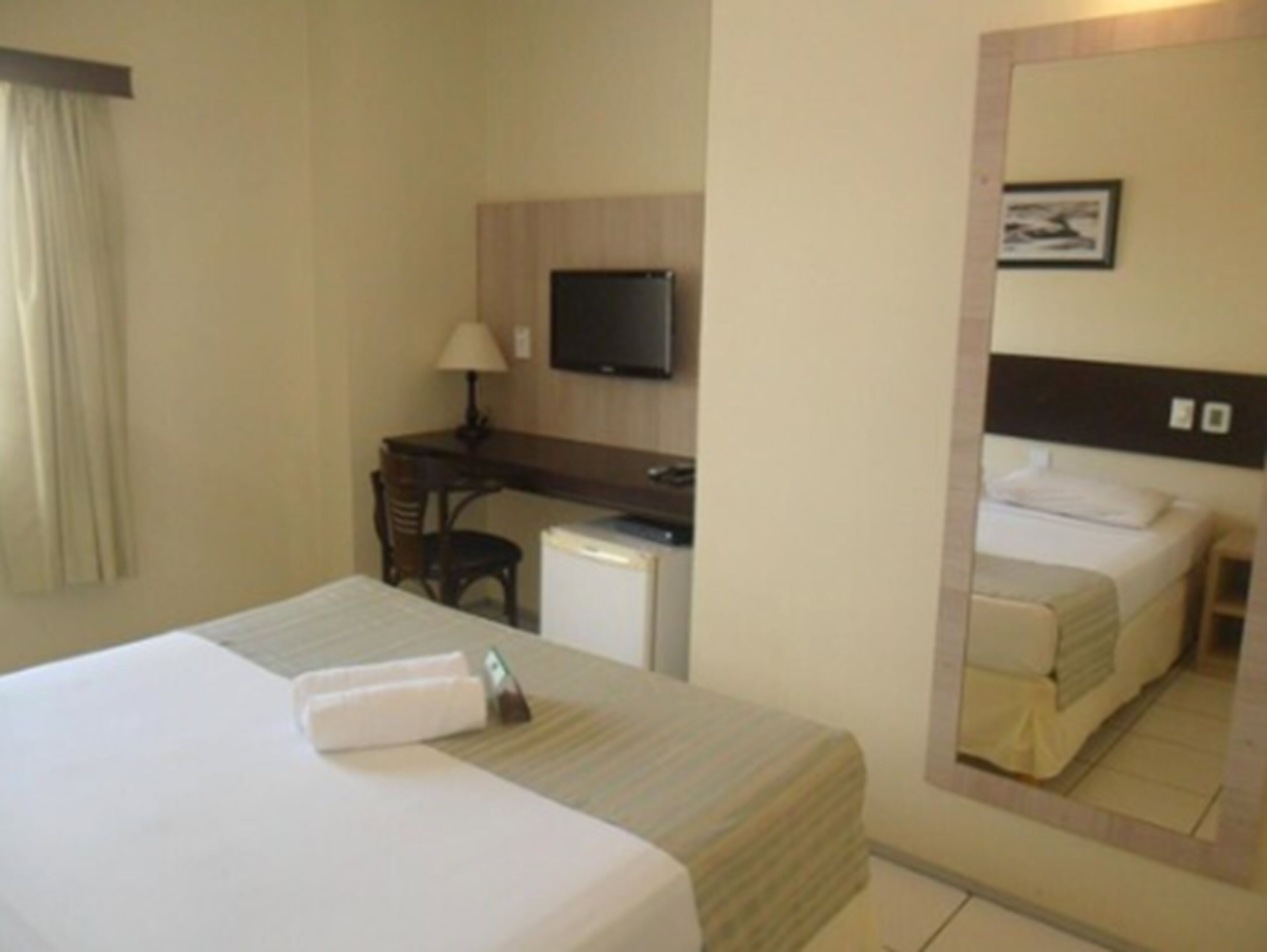 Une chambre d’hôtel comprenant un lit, un bureau avec une chaise, une télévision et un miroir.
