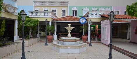 A courtyard with a central fountain, surrounded by buildings with balconies and a sign for 'Aulista'.