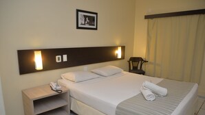 A hotel room with a bed, bedside table, and a nightstand with a phone. - Hotel Premier (São Luís)